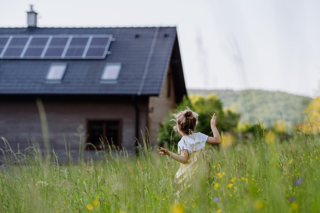 Rear view of little girl in front of family house with solar panels, concept of sustainable